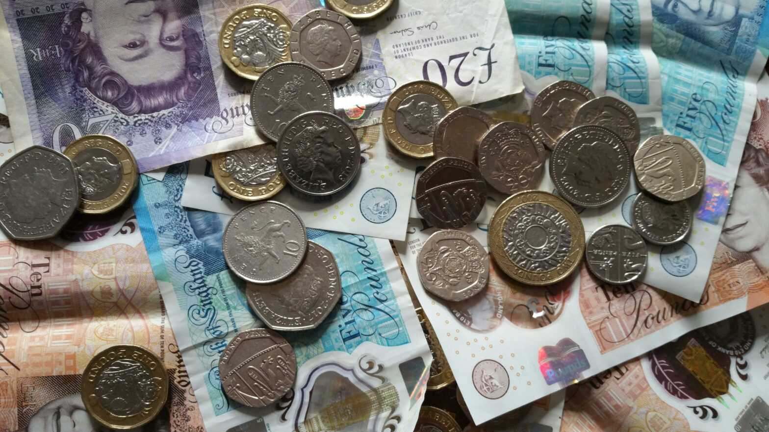 A selection of UK money laid on a table, with notes and coins of various amounts