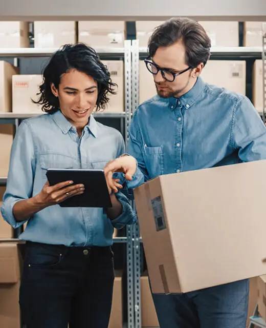 Man holding a box in a stockroom next to a woman holding a tablet and showing him something on the screen. Debt Refinancing.