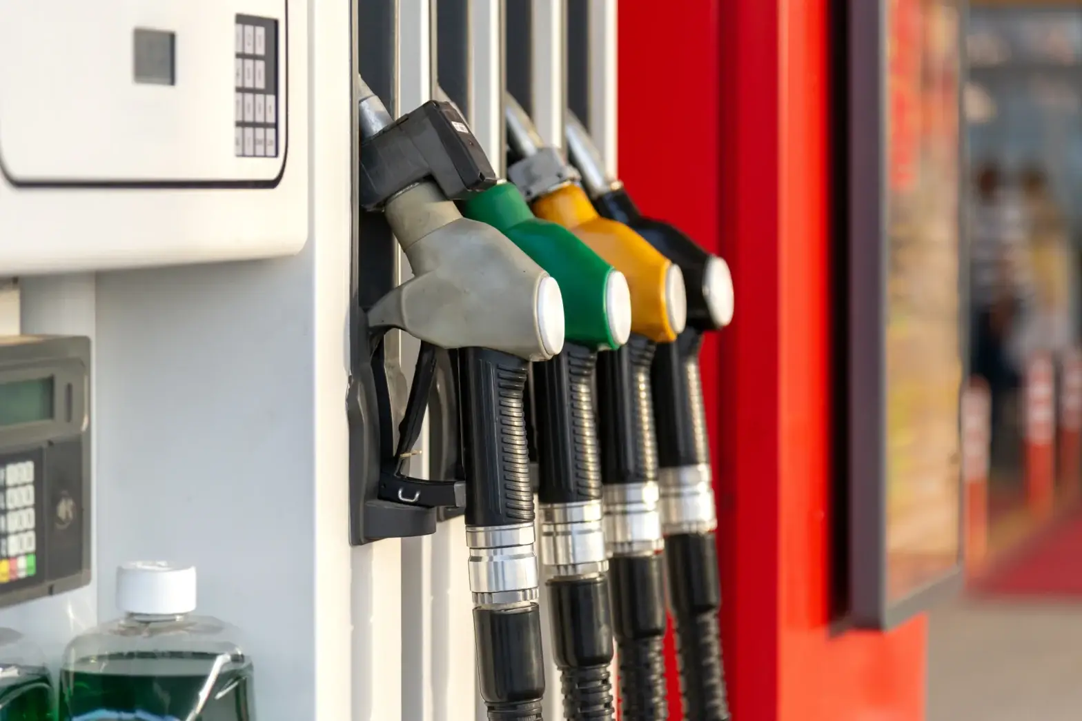 A close-up, selective focus shot of a row of fuel pump nozzles at a petrol station forecourt, featuring distinct grey, green, yellow, and black handles.
